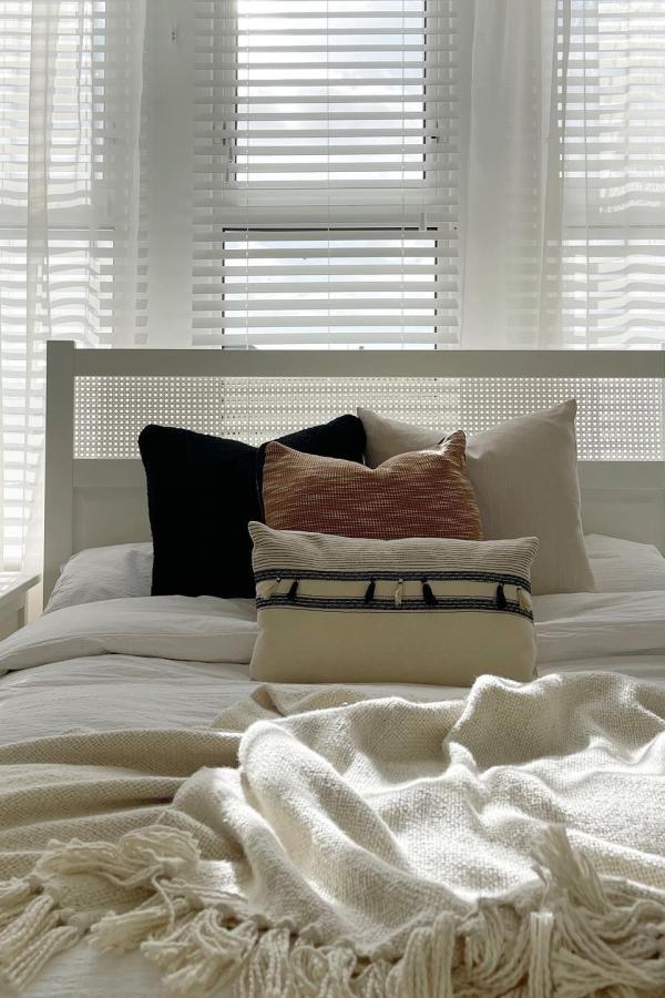 Woven cane headboard bedroom with neutral pillows and throws from @rooms_byrachel