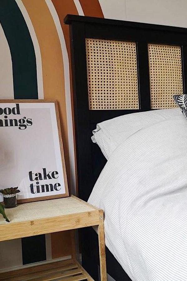 Black headboard with natural cane webbing panels from @our.home.on.cyril featuring striped bedding and wall art.