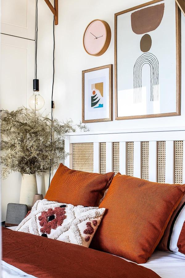 White headboard with cane webbing panels from @designbykornel. Rust colored bedding and abstract wall art complete the look.
