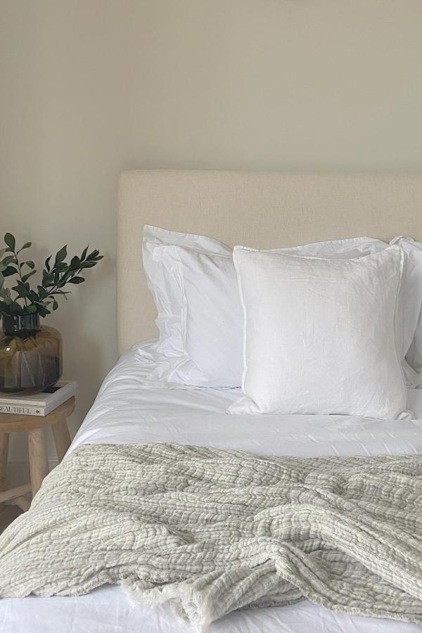 Neutral linen upholstered headboard from @north.manor. Cozy beige fabric adds warmth to minimalist bedroom styling.