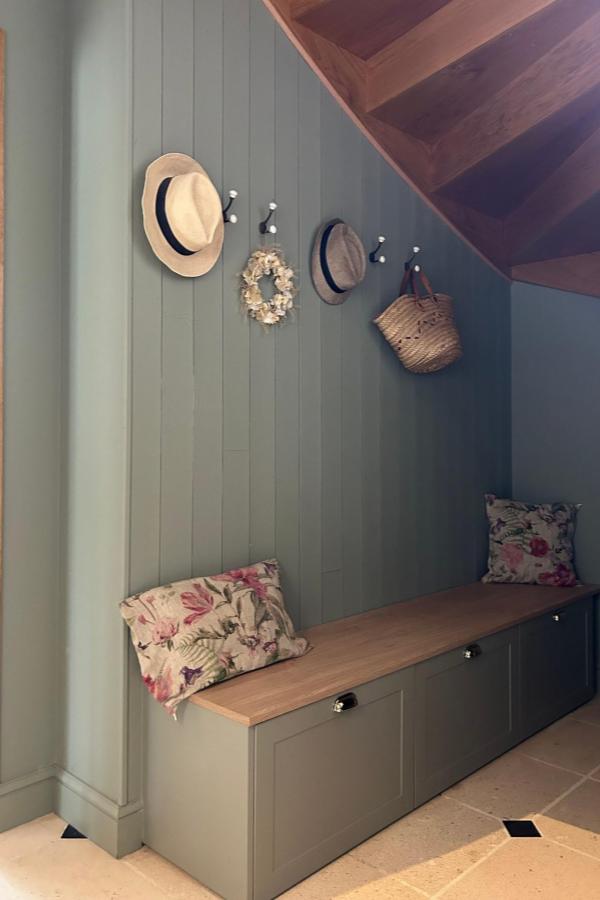 Sage green built-in bench storage from @plum.living showcasing creative ikea mud room ideas under staircase.