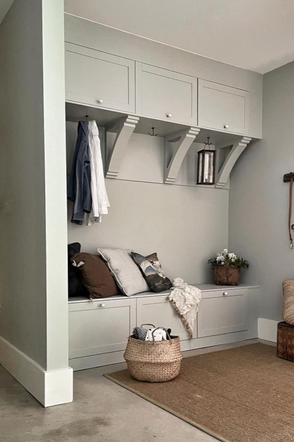 Built-in white storage bench and cabinets from @homeathand showcasing practical ikea mud room ideas with hooks and sage walls.