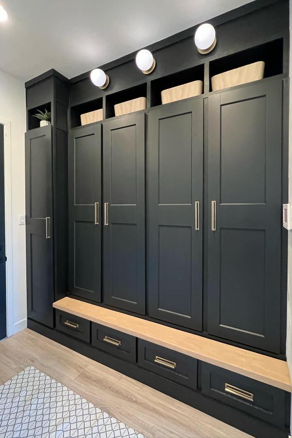 Dark green built-in mudroom lockers from @itsthelandofaus. Custom-looking storage wall with wooden bench and brass hardware.