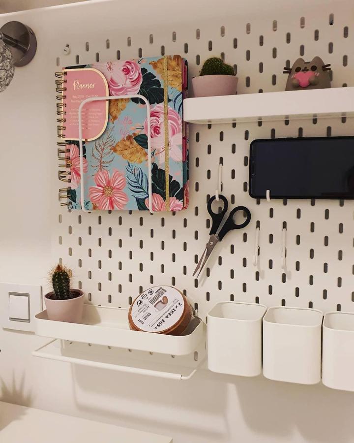 White pegboard planning station from @mydailyplanners. Organized shelves holding floral planners and supplies.