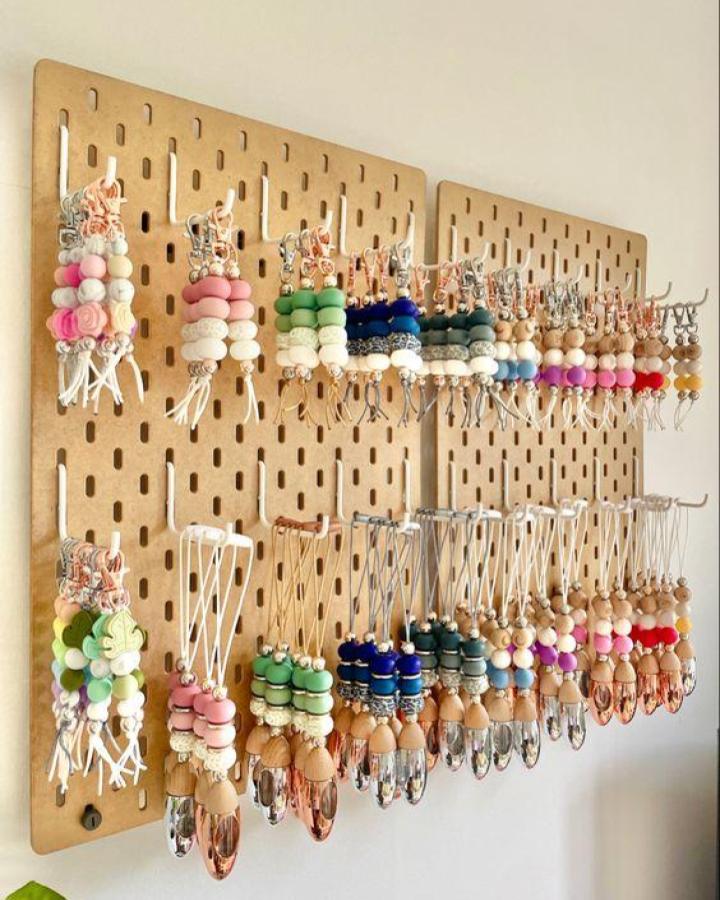 Natural wood pegboard display from @snowgumandbeads. Colorful silicone beads organized by color on metal hooks.