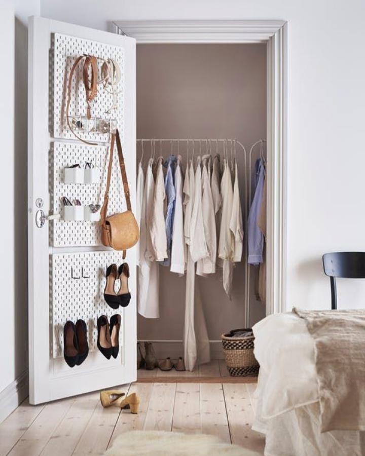 White pegboard mounted on closet door with shoes, bags and accessories organized on hooks from Ikea.