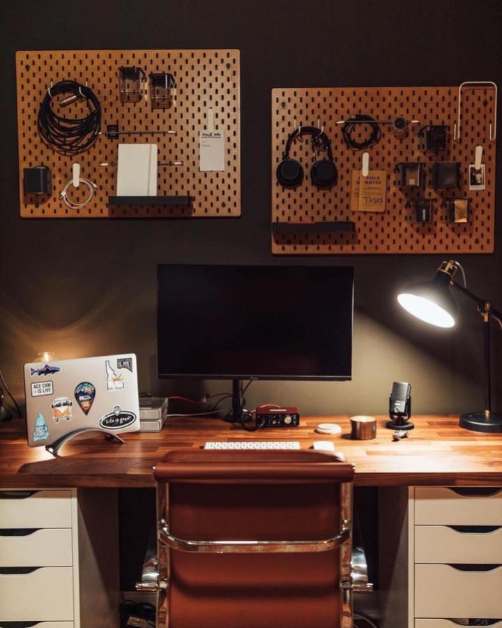 Honey-stained wooden pegboard setup from @productivespaces. Mounted above desk with organized tech accessories and cables.