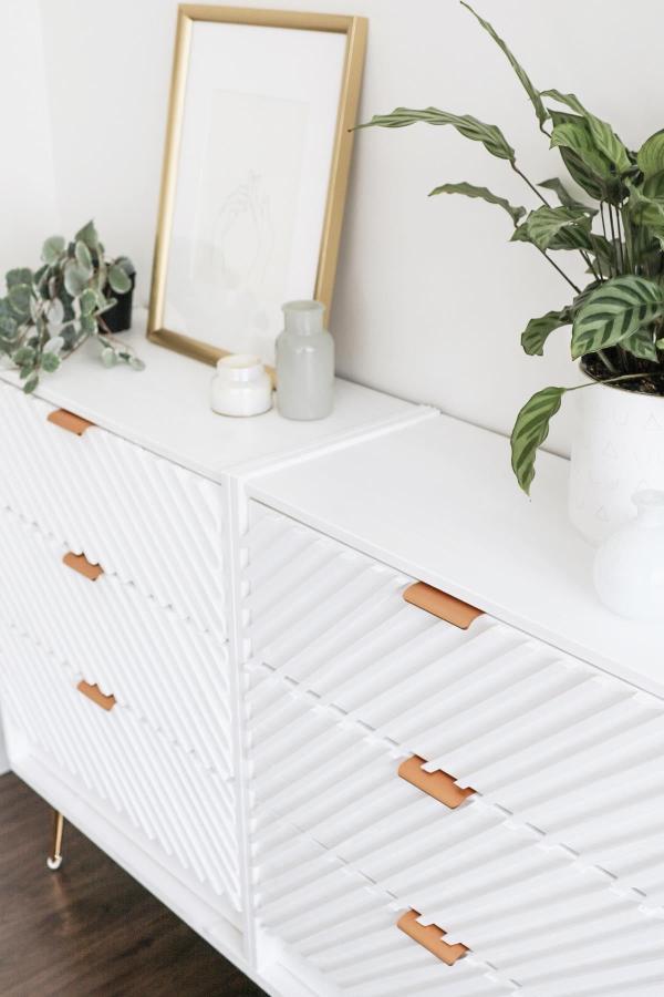White textured dresser from @akminteriordesign with copper leather handles and plant styling.