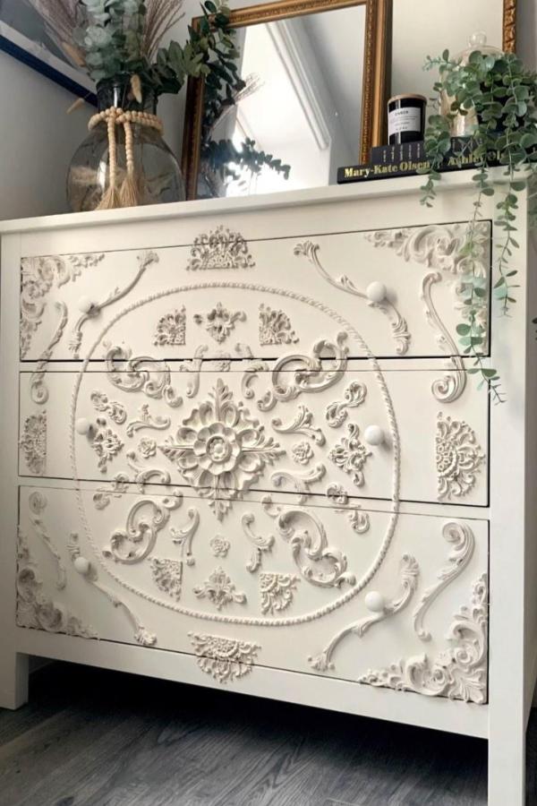 Ornate white dresser from @theflippedpiece featuring decorative appliques and floral medallion design.