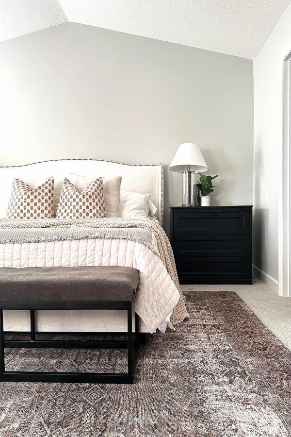 Black painted bedroom dresser from @homeonelleavenue serving as stylish nightstand beside neutral bed.