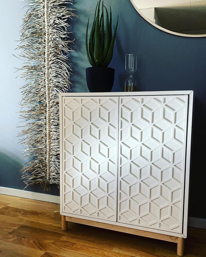 White geometric cabinet with 3D cube pattern doors from @frontcover.se. Natural wood legs elevate the design.