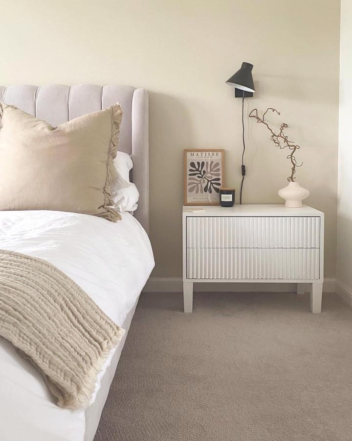 Fluted white nightstand from @kcinterior. Modern bedroom storage with wooden legs and textured paneling design.
