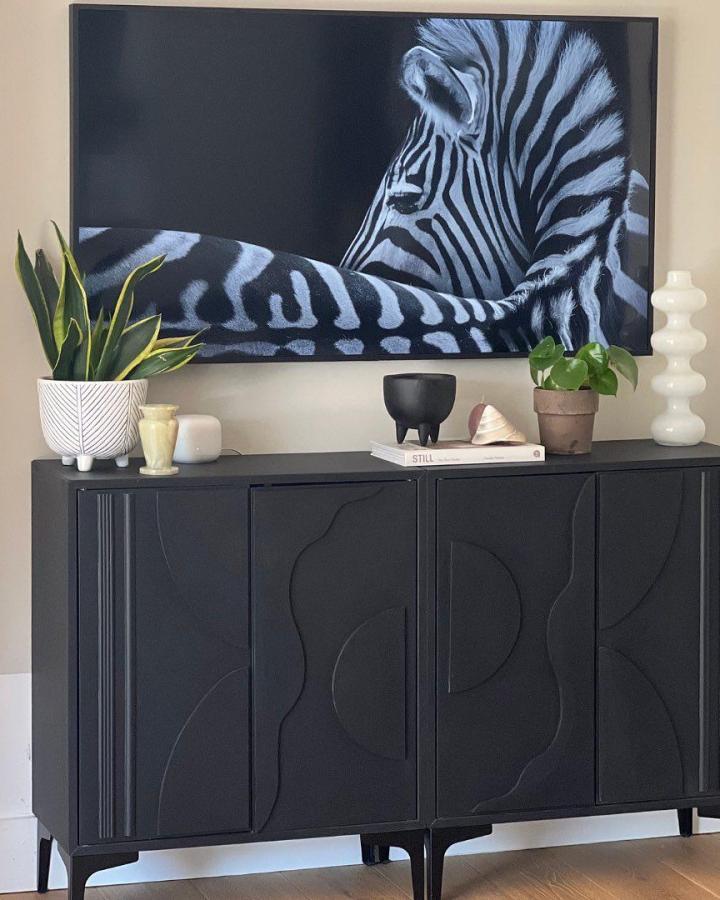 Black sideboard with curved decorative patterns from @our_bears_home. Zebra artwork and plants complete the styling.
