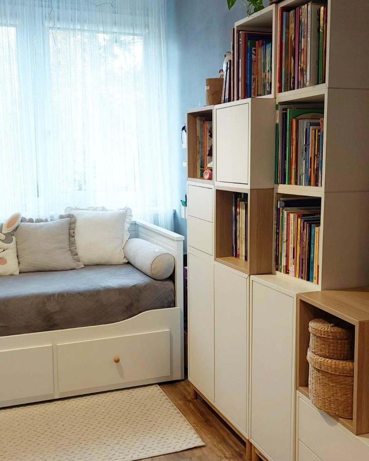 White stacked modular shelving system beside daybed from @sskuzik. Books organized in cube compartments with wicker storage baskets.