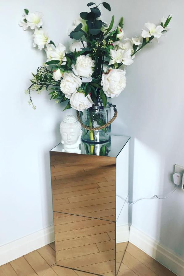 Reflective cube pedestal from @homeiswherethecathairis displaying white flowers in glass vase on wooden flooring.