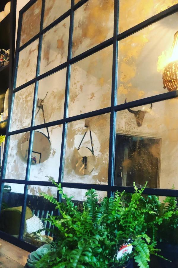 Antiqued mirror wall installation from @d.i.y.darling. Black grid framework with weathered glass panels creates industrial aesthetic.