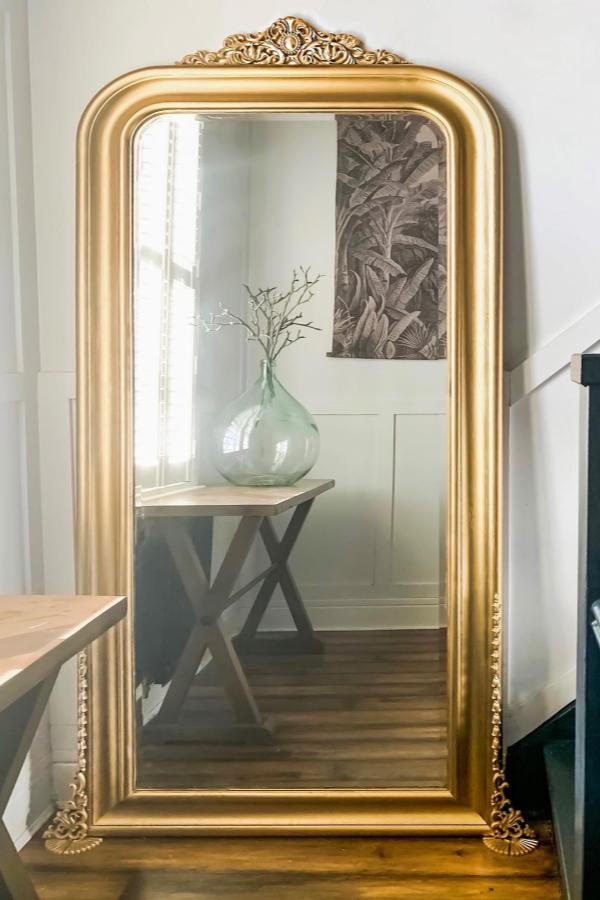 Ornate gold framed mirror from @mrs_macs_home leaning against white wall creating vintage glamour.