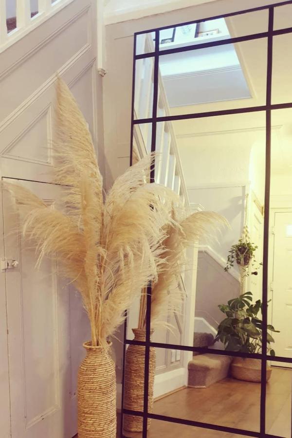 Black grid-framed hallway mirror from @our_snow_nest with pampas grass and woven baskets nearby.