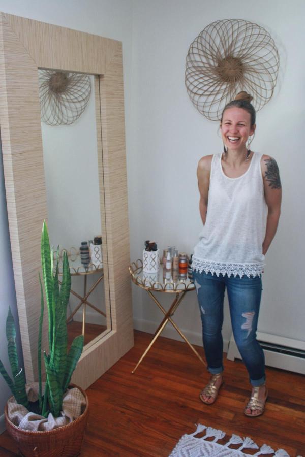 Bamboo-framed full-length mirror makeover from @elmariemade. Woman standing next to transformed IKEA mirror with natural grasscloth texture.