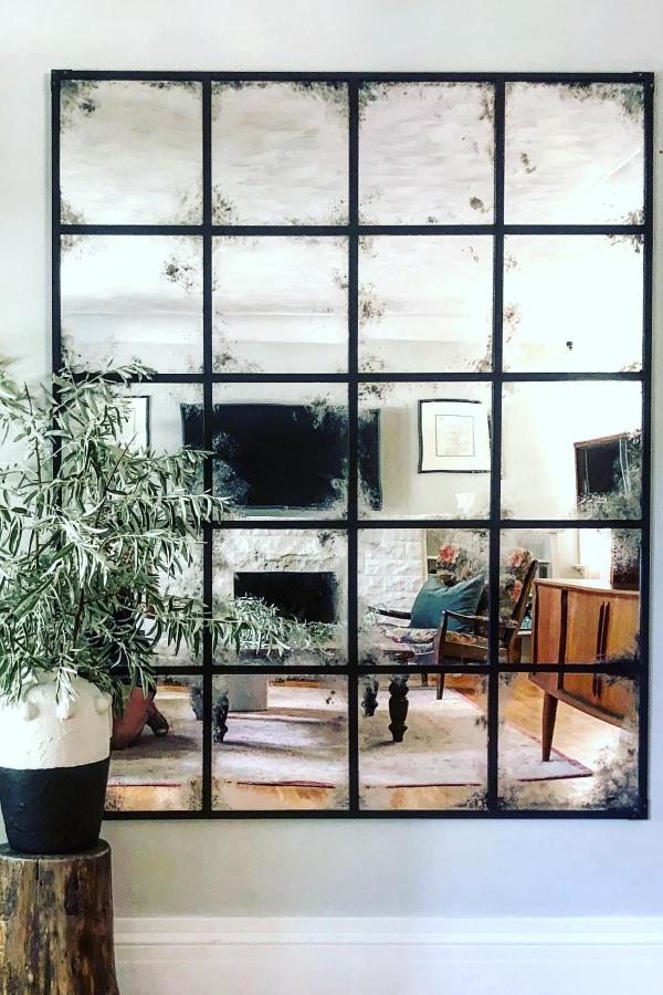 Large antiqued grid mirror with black metal frame from @alterboydesign. Weathered mirror panels create vintage industrial wall accent.