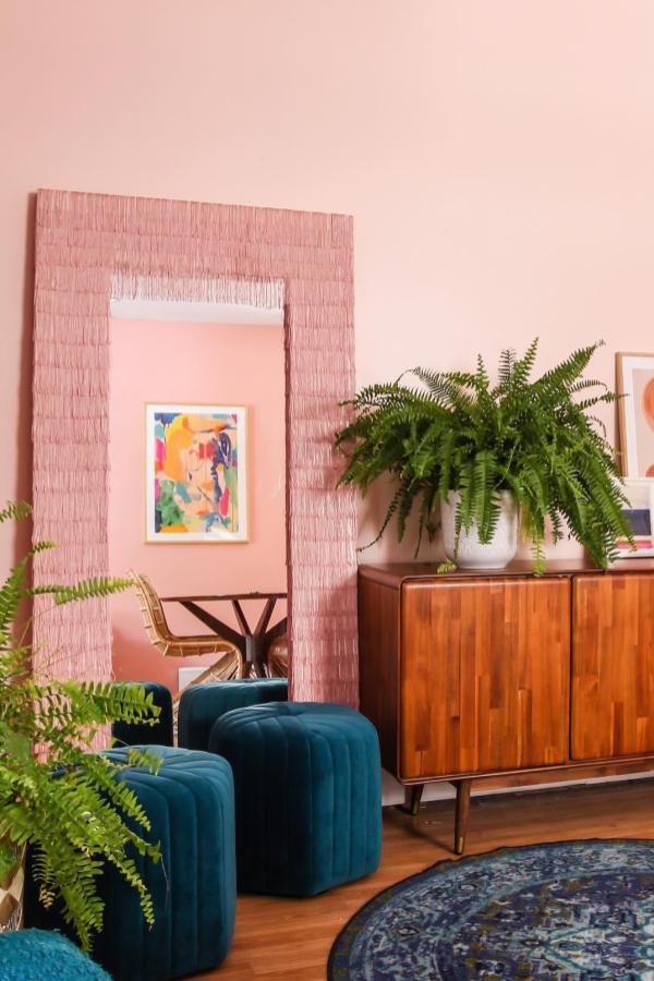 Pink fringe-wrapped mirror displaying colorful artwork in coral room showcasing creative ikea mirror hacks & ideas from @meganzietz