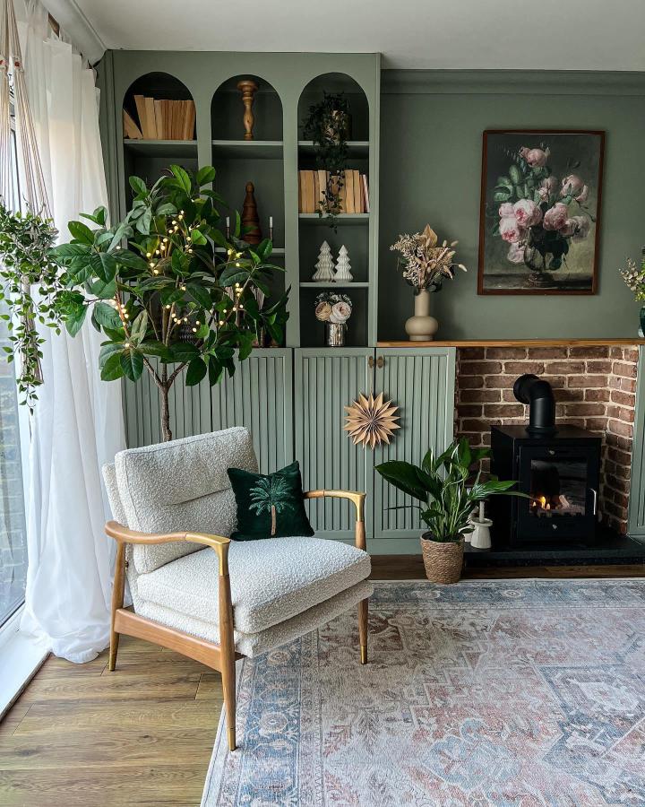 Sage green built-in bookcase with arched alcoves from @melaniejadedesign. Styled with plants and decorative objects in cozy living room.