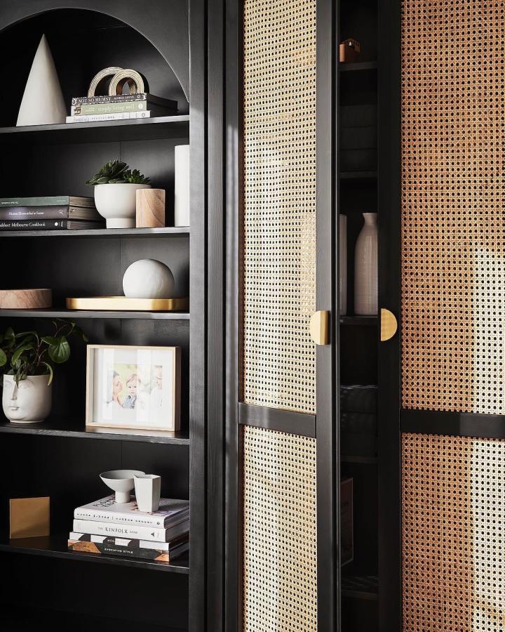 Dark built-in storage unit from @liberty.interiors featuring cane webbing doors and arched display shelving.
