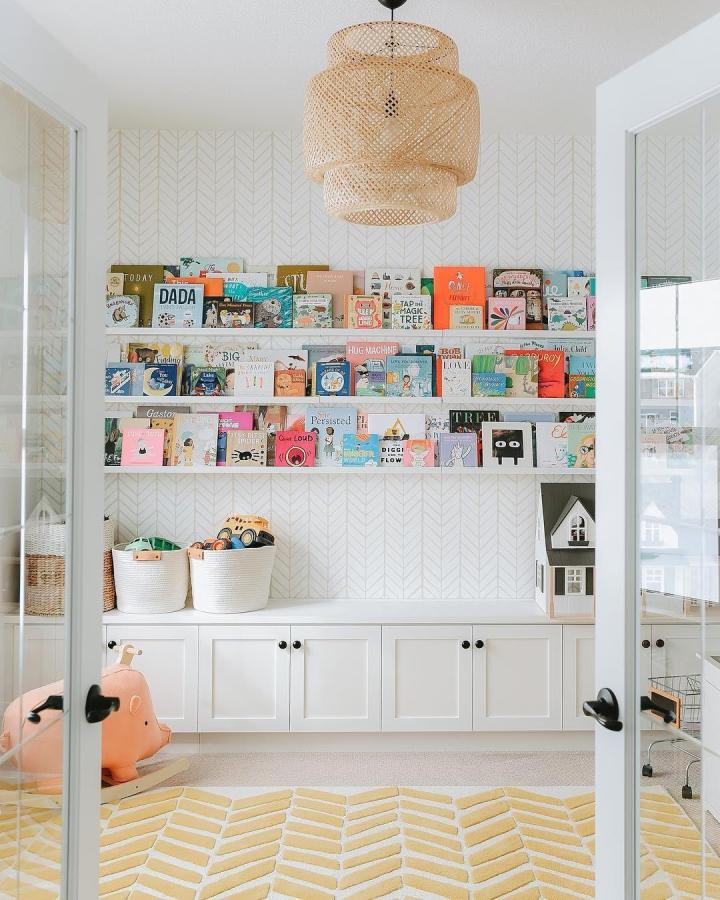 Bright playroom featuring ikea mosslanda ideas with colorful children's books displayed on white wall shelves above built-in storage.