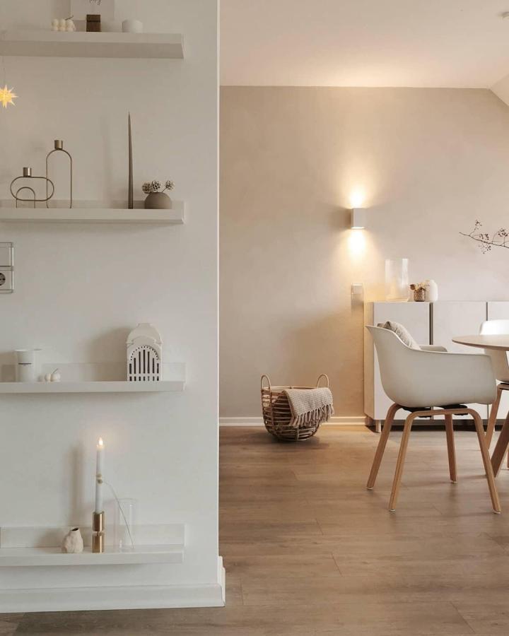 Minimalist white floating shelves from @alltagsschaetze displaying neutral decor items and candles in modern living room.