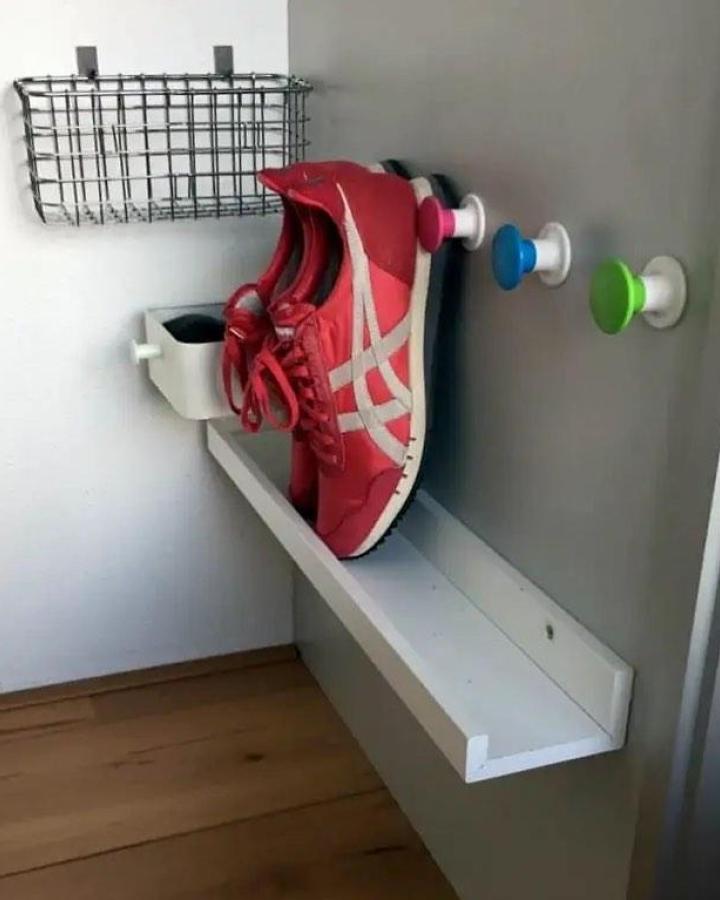 White entryway organization system from @ikeahackersofficial. Mosslanda shelf with colorful wall hooks for shoes and accessories.