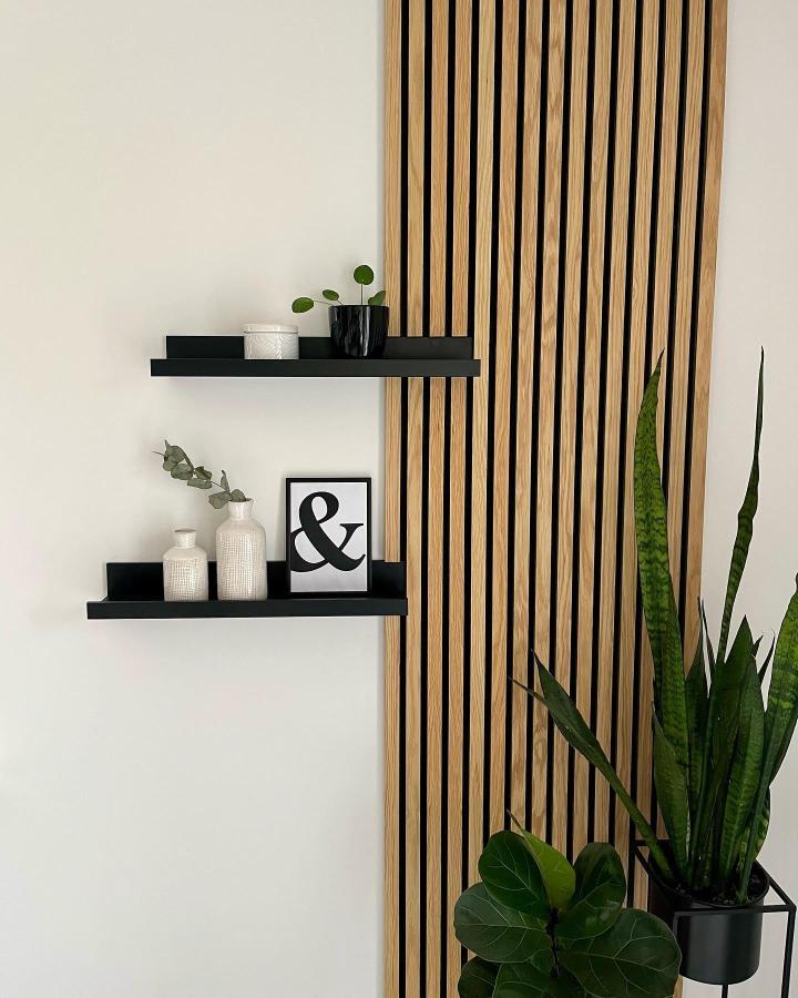 Modern black floating shelves mounted on wooden slat accent wall with minimal decor and plants.