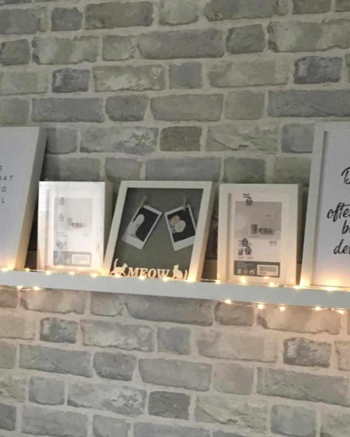 White picture ledge display with fairy lights showcasing ikea mosslanda ideas from @chase_downham_tw against grey brick wall.