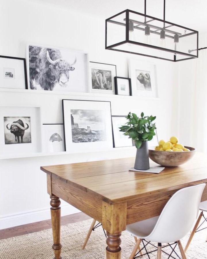 Monochrome gallery wall display from @jmwearing featuring layered black framed prints above wooden dining table.