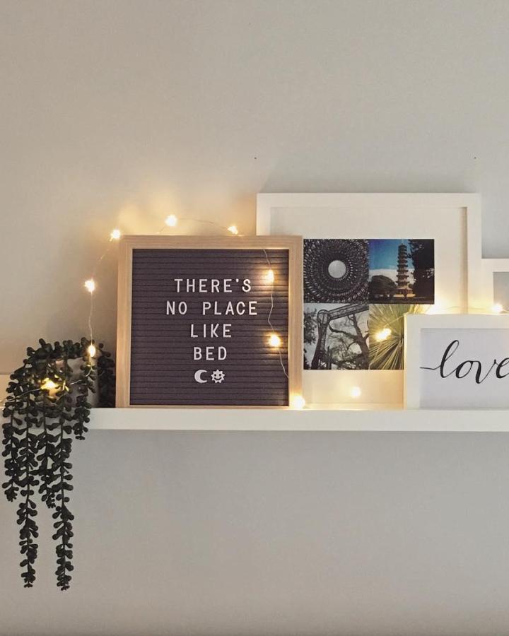 Cozy bedroom shelf display from @suzisooz. Letter board and fairy lights create warm ambiance.