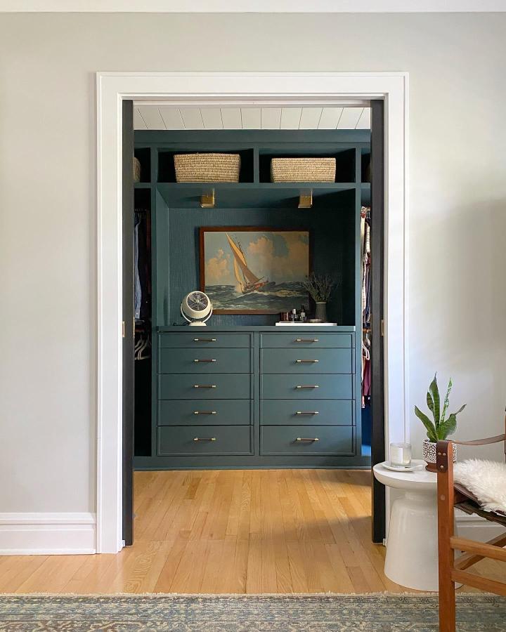 Deep teal painted Pax wardrobe with brass hardware and woven baskets from @jarod_sabatino_interiors. Vintage sailboat art anchors the display.