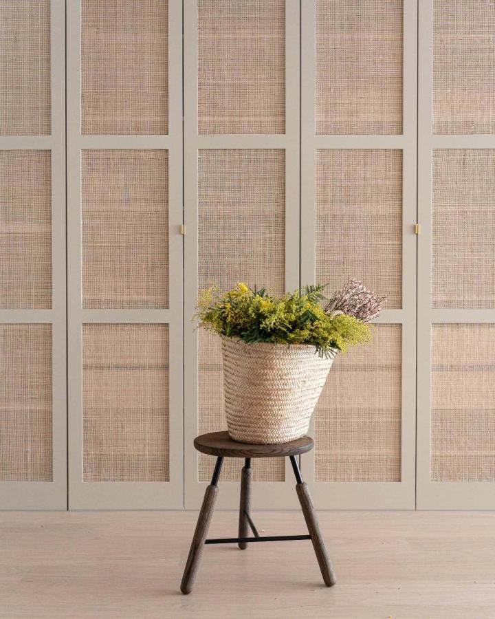 Sage green wardrobe with natural cane webbing door panels from @fronteriors. Woven basket with greenery on wooden stool