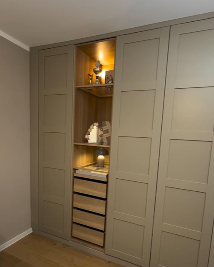 Sage green Pax wardrobe with shaker panel doors and lit display shelving from @livinghausvibes. Wooden drawer inserts below open shelves.