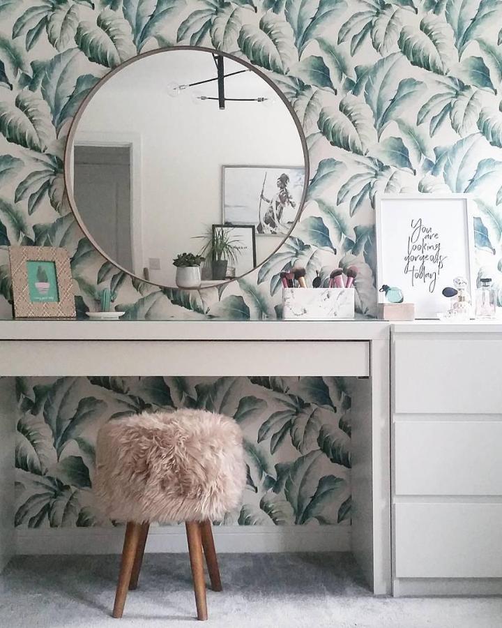 Tropical leaf wallpaper vanity setup from @caffeineandcacti. Pink fuzzy stool complements botanical green patterns beautifully.