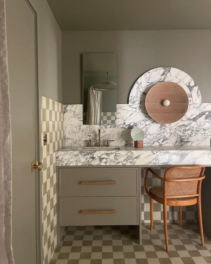 Contemporary marble vanity setup from @sarahshermansamuel. Sage green Ikea cabinets with geometric tile backsplash.