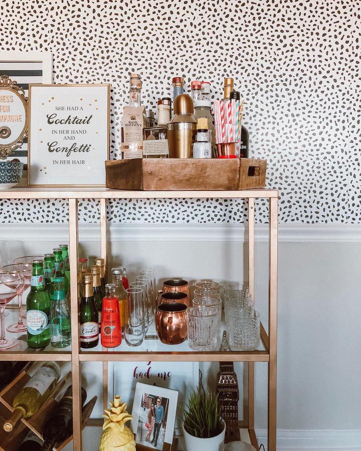 Gold and copper bar cart from @rachelmrudy. Mixed metallic bottles and glassware on white shelving.