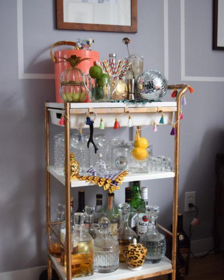 Gold-painted Ikea Bygel bar cart from PMQ for Two with tassel garland and disco ball accents.