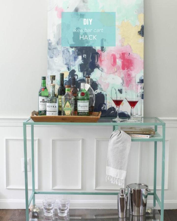 Mint green metal bar cart from Style me Pretty displaying liquor bottles and glassware beneath abstract art.