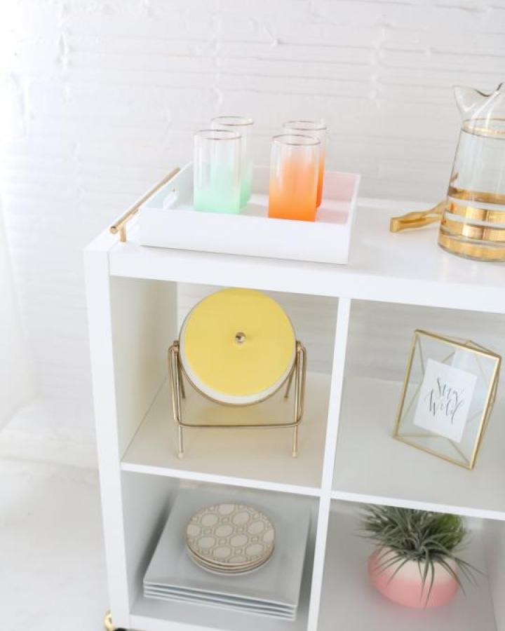 White Kallax cube storage cart from Sugar and Cloth with brass wheels and colorful glassware display