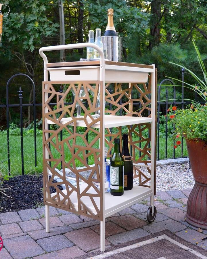 Blush pink Ikea Bygel trolley from @myoverlays with geometric wood panel sides holding champagne bottles outdoors.