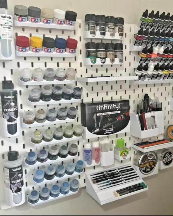 White pegboard paint organizer for ikea craft room ideas from 3DShrimping with angled shelves holding model paints and brushes.