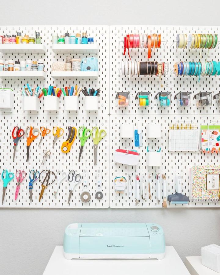 White pegboard craft wall from @heyletsmakestuff with colorful ribbon, scissors, and organized supplies displayed vertically.
