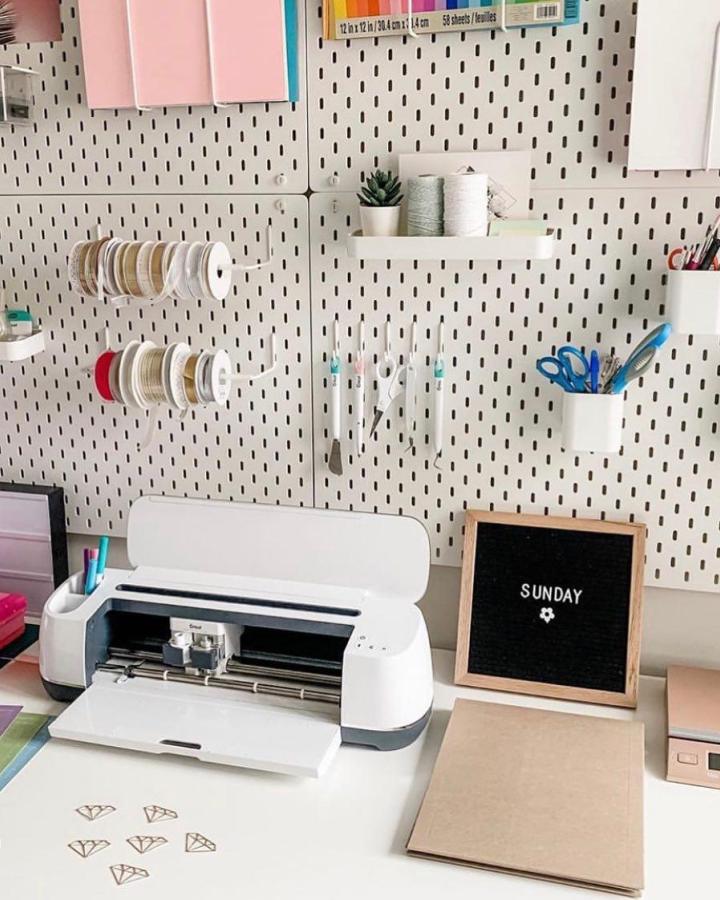White pegboard craft station from @caralynkempner with ribbon storage and hanging organizers above cutting machine.
