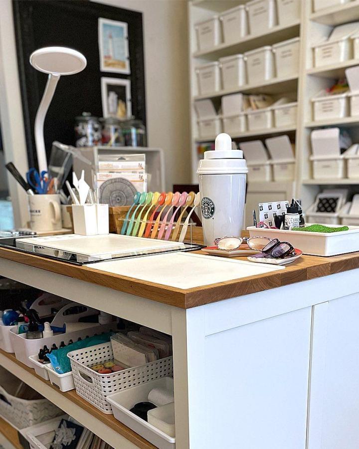 White craft island from @ribbongirls with butcher block top and organized storage shelves below.