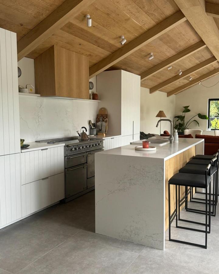 Marble-effect waterfall island with oak panel from @our_bears_home beneath exposed timber beam ceiling.