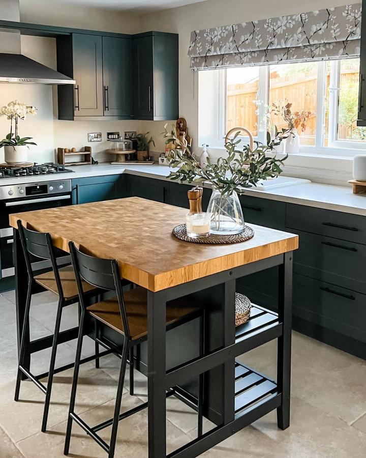 Black framed island with butcher block top from @boos_home in green kitchen with bar stools.